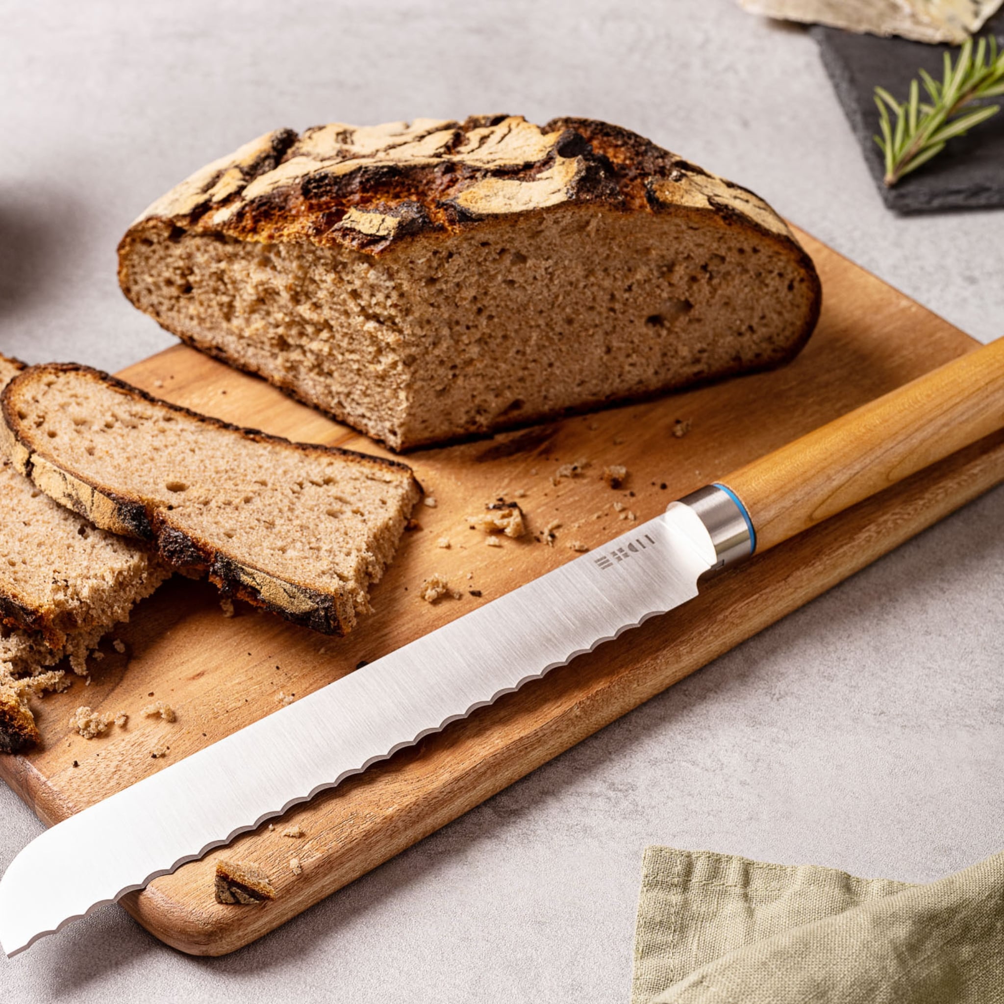 Couteau à pain ETCH avec lame crantée posée devant une miche de pain rustique tranchée sur planche en bois, mise en scène gourmande et artisanale