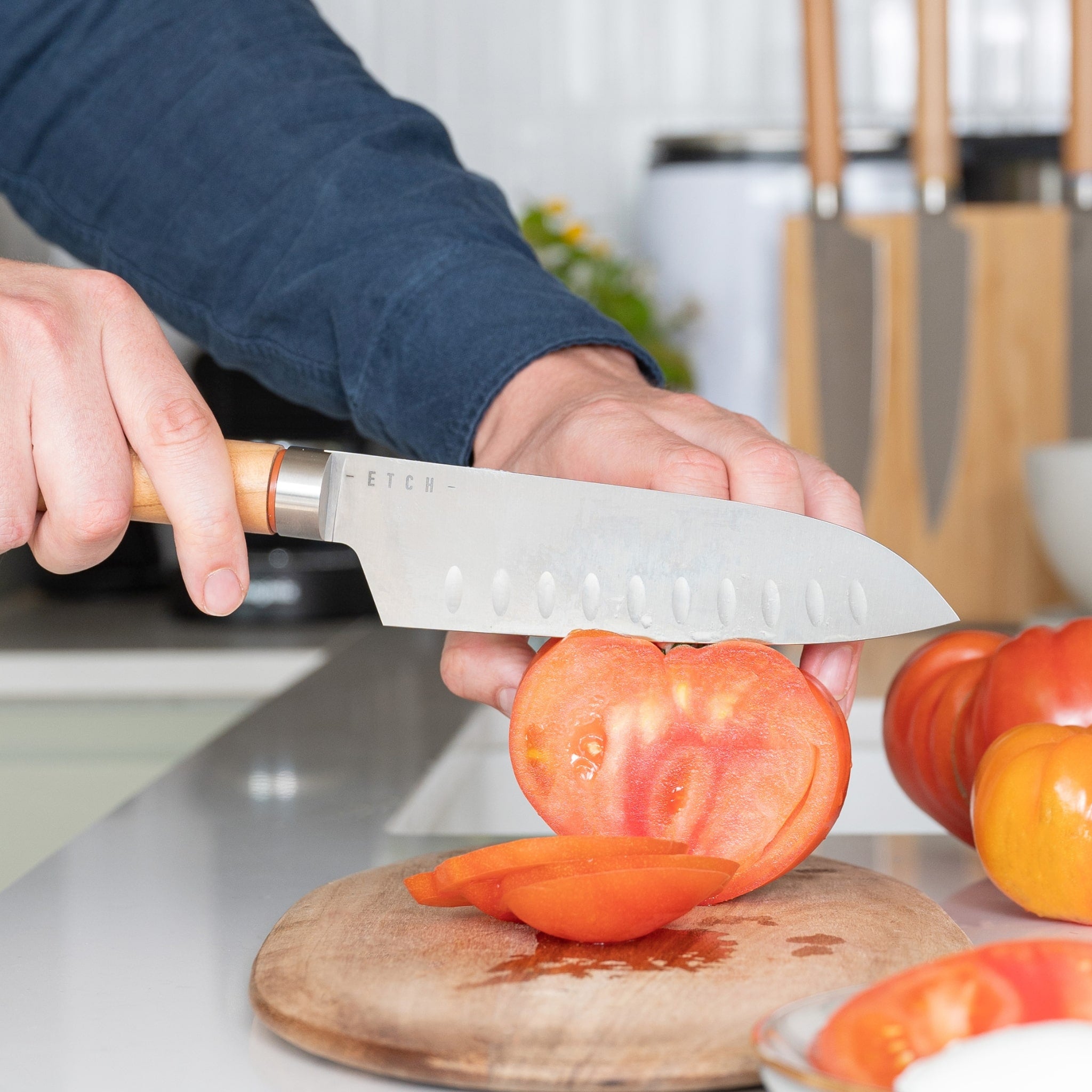 Couteau Santoku ETCH tranchant une tomate cœur de bœuf, gestuelle fluide et lame alvéolée pour coupe nette