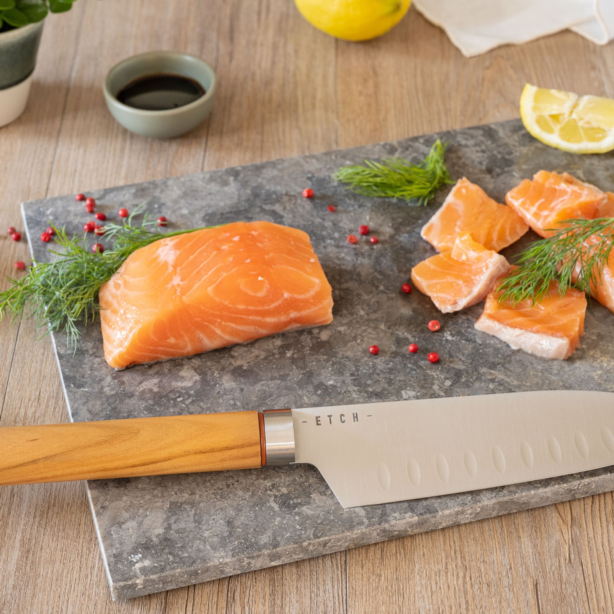 Couteau Santoku ETCH en présentation avec pavé de saumon cru et dés réguliers, sur planche en pierre, illustrant une découpe nette et professionnelle